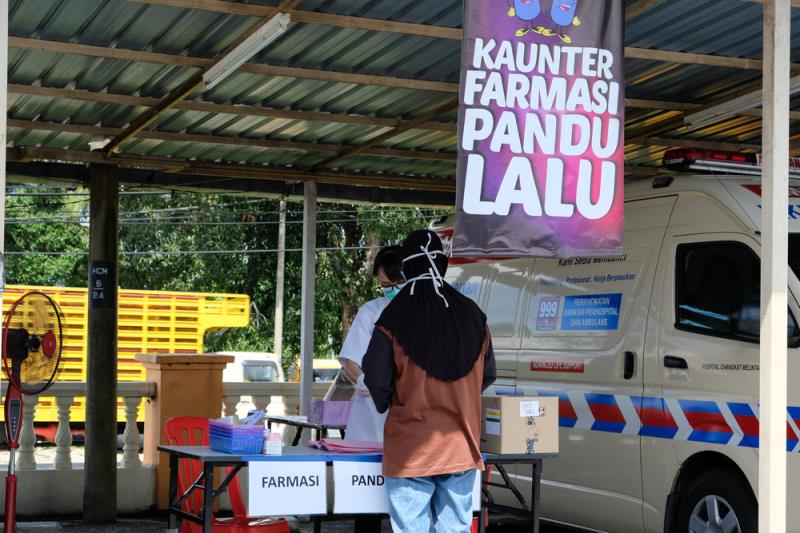 A pharmacist distributes medicines at a drive-through counter outside Hospital Changkat Melintang, Perak, to reduce entry int